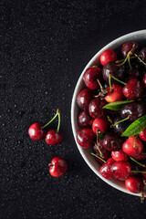 Fresh sweet cherries in a white bowl on a black background, top view.