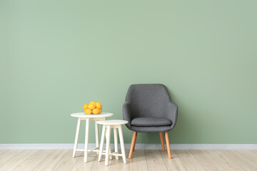 Stylish armchair with tables and lemon fruit near color wall in living room