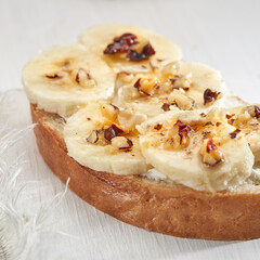 Sandwich with banana slices sprinkled with nuts close up on a white wooden table.
