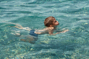 Child boy swimming in clear transparent sea.