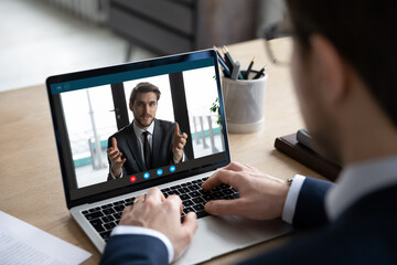 Back view of businessman sit at desk have video call on laptop with male business partner, man...