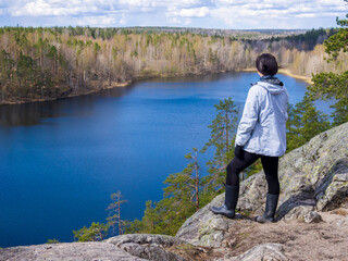 Fototapeta na wymiar Girl tourist stands on a rock looks at the lake