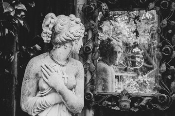A statue looks into a mirror in an overgrown garden. This is a black and white image 