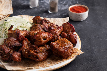 Juicy pork meat cooked on skewers. Pork meat on a plate with red sauce. Text space
