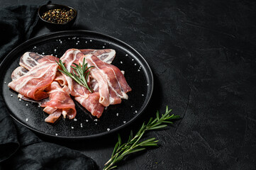 Pork bacon on a black plate. Farm organic meat. Black background. Top view. Space for text