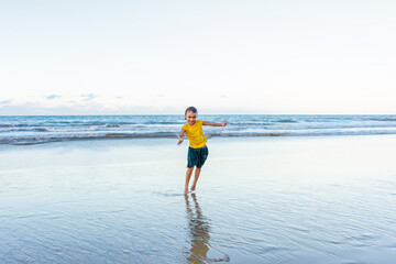 Fototapeta na wymiar Child dancing cheerfully on the beach with shadows