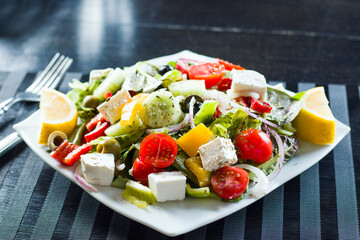 Vegetable salad on the plate, tomatoes, green salad, cheese, lemon and olive, other vegetables.