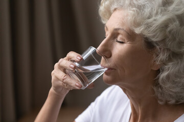 Thirsty elderly woman drink clear pure mineral water from glass, take daily dose for body balance...