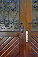 Old door in antique style with wrought-iron bars and a window, close-up. Door knocker on a wooden door. Selective focus