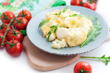Baked cauliflower and tomatoes with cream-garlic sauce on white background
