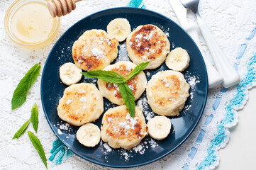 Cottage cheese pancakes, syrniki with banana and mint in blue plate. Breakfast for child. Top view