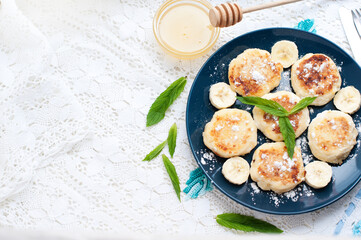 Cottage cheese pancakes, syrniki with banana and mint in blue plate. Breakfast for child. Top view