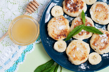 Cottage cheese pancakes, syrniki with banana and mint in blue plate. Breakfast for child. Top view