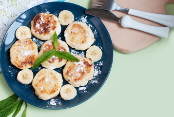 Cottage cheese pancakes, syrniki with banana and mint in blue plate. Breakfast for child. Top view