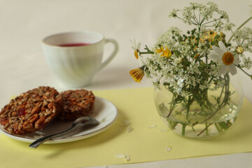 A bouquet of wild flowers with cookies and a Cup of tea on the table, white background, side view, selective focus.