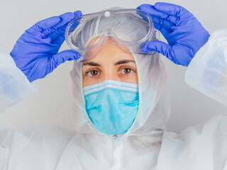 Young woman doctor in uniform, medical cap and mask, close-up portrait. She puts the glasses. Coronavirus concept.