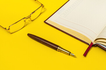 Gilt pen and glasses rests near a open notebook for notes or writing text