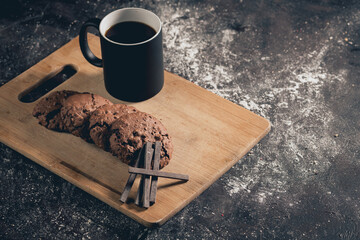 Homemade chocolate chip cookies with chocolate bars with coffee, on wooden board and black table