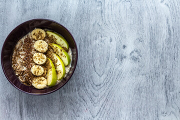Plate of oatmeal with apple, banana, cinnamon and flax seeds stands on a gray wooden background. Top view. Copy space for text. Healthy breakfast concept