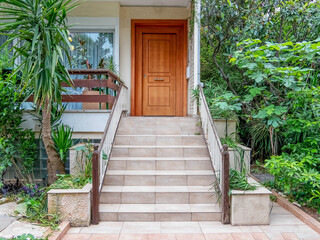 stairs of a family house entrance with natural wood door and flowerpots