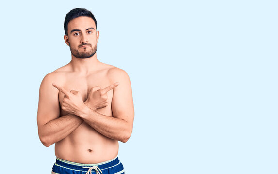 Young handsome man wearing swimwear pointing to both sides with fingers, different direction disagree