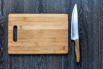 Wooden cutting board and a knife liyng on a dark background. Top view. Copy space for text