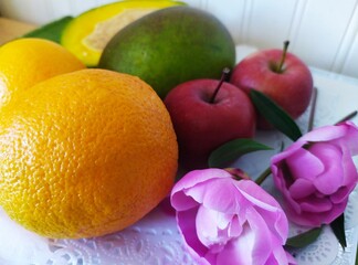 Still life of fruits red apples ogange oranges green mango and pink peones flowers on the white plate