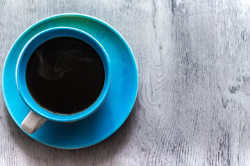 Blue cup of hot coffee on a saucer stands on a gray wooden background, top view. Copy space for text.