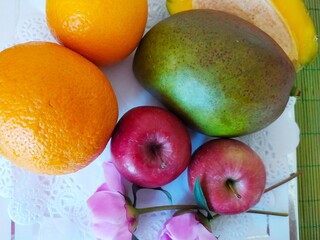 Still life of fruits red apples ogange oranges green mango and pink peones flowers on the white plate
