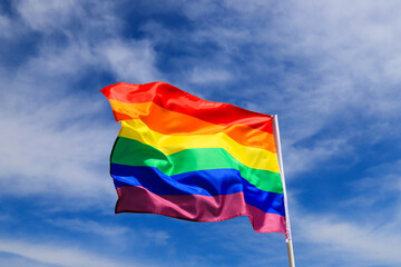 Realistic rainbow flag of an LGBT organization waving in a sky. LGBT pride flags include lesbians, gays, bisexuals and transgender.