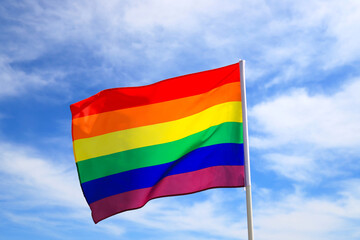 Realistic rainbow flag of an LGBT organization waving against a blue sky. LGBT pride flags for lesbians, gays, bisexuals and transgender.