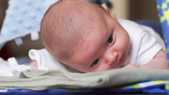 2 months old little baby boy struggling, trying to hold his head up during tummy time. Baby lifting head while lying on belly on playing mat. Flat head preventing exercise.