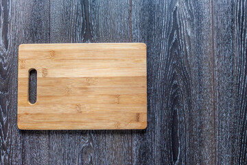 Wooden cutting board liyng on a dark wooden background. Top view