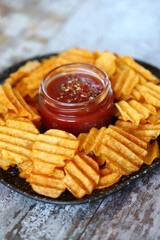 Selective focus. Plate with spices sauce and corrugated potato chips. Unhealthy food. American snack.