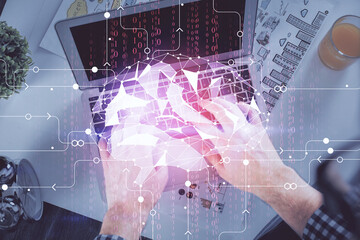 Double exposure of man's hands typing over computer keyboard and brain hologram drawing. Top view....