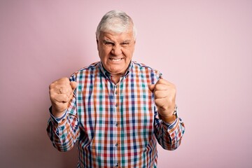 Senior handsome hoary man wearing casual colorful shirt over isolated pink background angry and mad raising fists frustrated and furious while shouting with anger. Rage and aggressive concept.