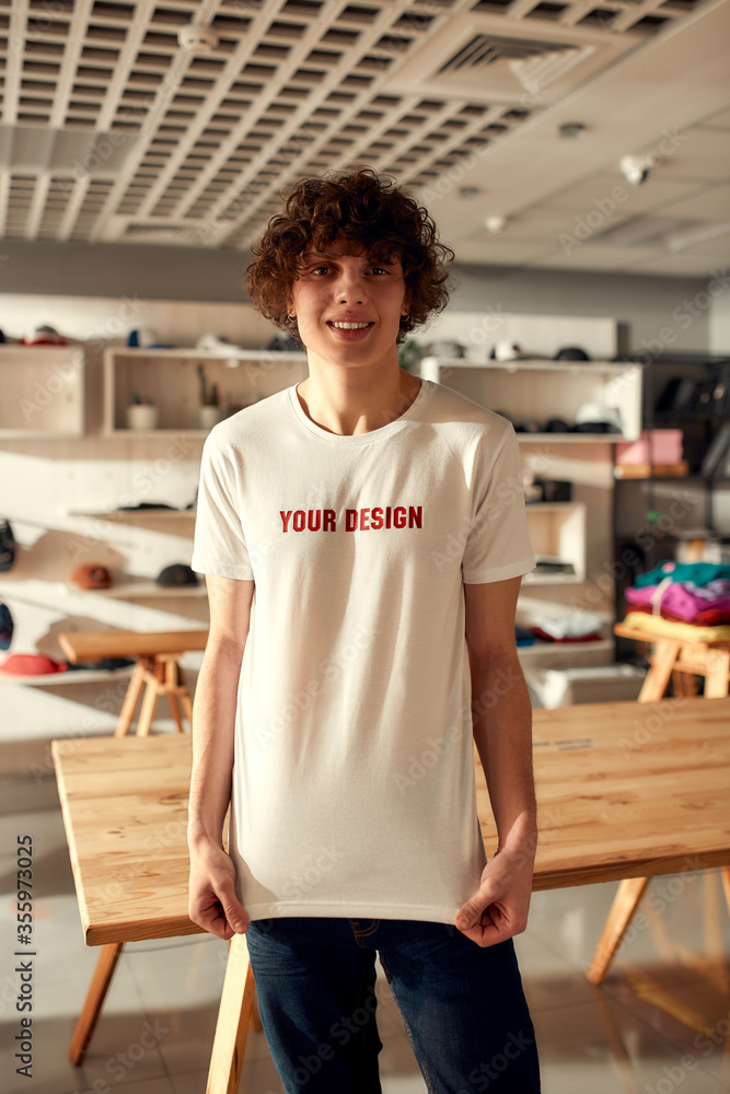 Wall mural design solutions. young man smiling at camera, while trying on printed t shirt, standing in the stor