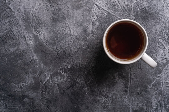 One ceramic cup with hot black tea, drink in white teacup on textured dark stone background, top view copy space
