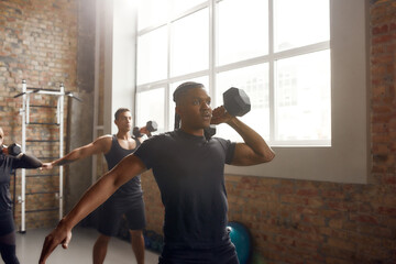 Prepare hard. Athletic man lifting dumbbell while having workout at industrial gym. Group training, teamwork concept