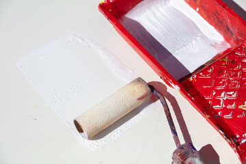 Red tray with white paint and a paint roller on a white surface