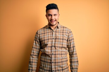 Young handsome man wearing casual shirt standing over isolated yellow background winking looking at the camera with sexy expression, cheerful and happy face.