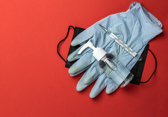 Virus protection. Medical surgical mask, sanitizer gel, thermometer and lab gloves on red background. Risk Coronavirus disease COVID-19 pandemic concept. Medical respiratory bandage face