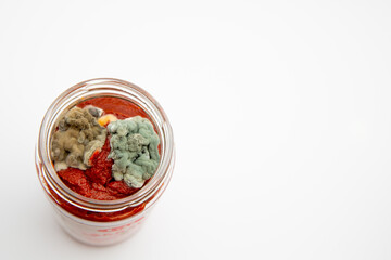 Close up shot of mouldy tomato paste in a glass jar isolated on white background with copy space