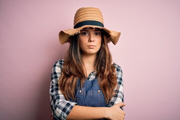 Young beautiful brunette farmer woman wearing apron and hat over pink background skeptic and nervous, disapproving expression on face with crossed arms. Negative person.