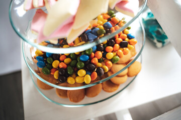 Candy bar. Close up of glass multi-tier plate with various sweets. Focused on colorful chocolate candies. Celebration, party, birthday or wedding