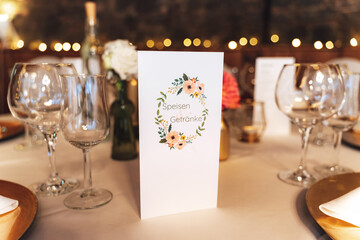 Festive table decoration. Close up of standing paper menu and arrangement of glassware....