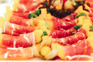 Closeup of tray with juicy slices of yellow melon rolled into ham. Self-service buffet table. Selective focus. Celebration, birthday, party, wedding