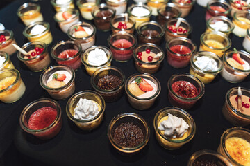 Top view rows of glasses with sweet vanilla, chocolate or fruit dessert. Self-serving buffet table. Selective focus. Celebration, party, wedding