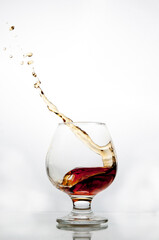 Splashes of cognac in a glass on a white background