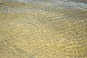 Abstract background of the ripples on water at the beach. Transparent sea water. Soft wave of ocean on sandy beach. Yellow background.
